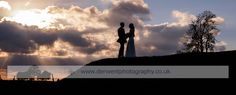 two people standing on top of a hill with the sun shining through clouds behind them