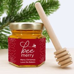 a jar of honey with a wooden spoon next to it and pine branches in the background