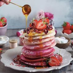 a stack of pancakes with strawberries and syrup being drizzled on top