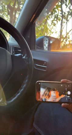 a person holding a cell phone in their hand while sitting in the driver's seat of a car