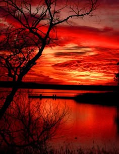 the sky is red and orange as it sits over water with trees in front of it