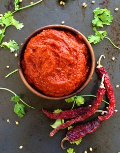 a bowl filled with red sauce next to some chili peppers