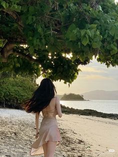 a woman walking on the beach under a tree