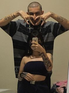 a man taking a selfie in front of a woman with tattoos on her arms