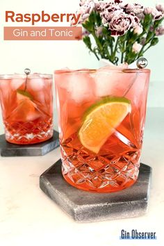 two glasses filled with gin and tonic sitting on top of a marble tray next to flowers