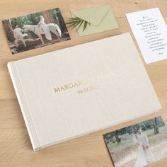 a wedding album with photos and an envelope on a wooden table next to two cards