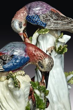 two colorful birds perched on top of each other next to leaves and flowers in front of a black background