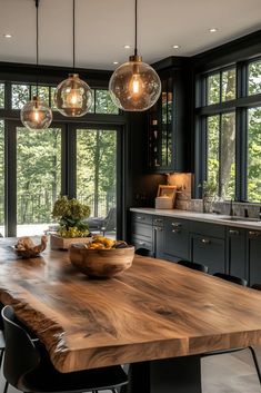 a large wooden table in a kitchen with black cabinets and lights hanging from the ceiling