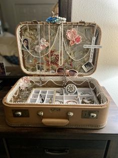 an open suitcase sitting on top of a wooden table next to a mirror with jewelry in it