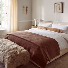 a bedroom with a large bed covered in brown and white blankets next to a window