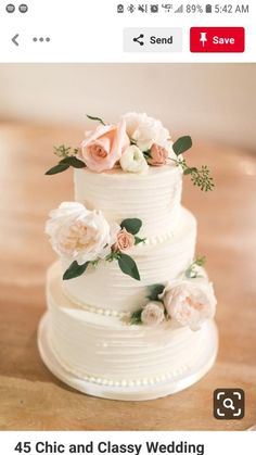 a three tiered white cake with pink flowers on top and greenery around the edges