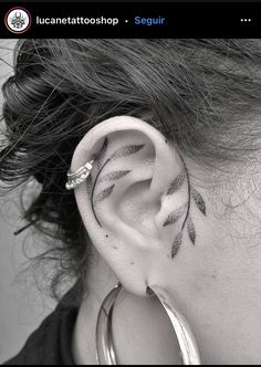 a close up of a person's ear with leaves on it and an arrow tattoo behind the ear