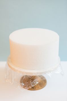 a white cake sitting on top of a table covered in plastic wrap and wooden buttons