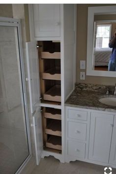 a person taking a photo of a bathroom with white cabinets and marble counter tops, while another man takes a selfie in the mirror