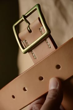 a person holding onto a brown belt with holes on it and a square buckle in the center