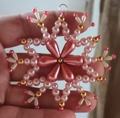 a hand holding a pink and gold beaded ornament in it's palm