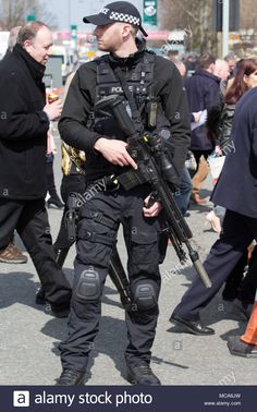 an armed police officer on duty in the middle of a crowded street with people walking around