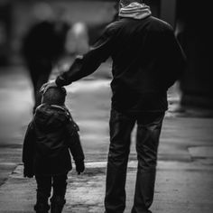 a man walking down the street with a small child on his back and an adult holding hands