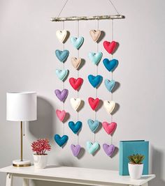 a white table topped with a lamp next to a wall mounted heart mobile hanging on it's side