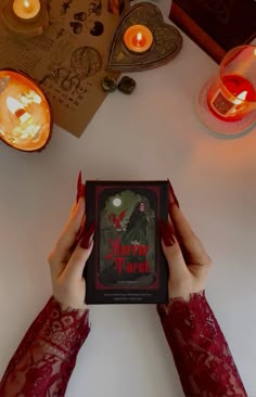 a person holding up a book in front of some candles and other items on the table