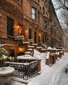 a snow covered sidewalk in front of a row of brownstone buildings with lights on