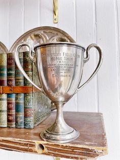 a silver trophy sitting on top of a wooden shelf next to books and a clock