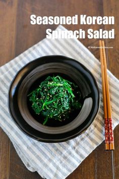 a black bowl filled with spinach and chopsticks