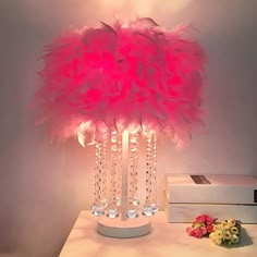 a pink lamp that is on top of a table next to some books and flowers