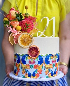 a person holding a decorated cake with oranges and flowers