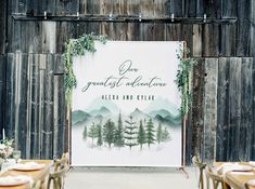 a wedding sign with greenery on it and place settings in front of a wooden wall