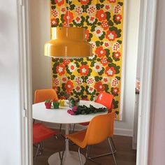 a white table with orange chairs and a yellow lamp hanging from the ceiling over it