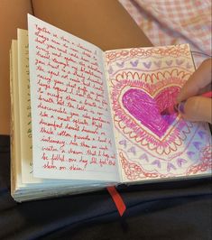 an open notebook with writing on it and a pink heart in the middle is held by someone's hand