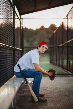 a young man sitting on a bench holding a baseball bat and wearing a red bandana