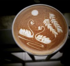 a cappuccino with an image of swans on the bottom and leaves in the middle