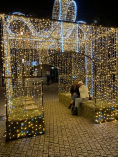 two people sitting on a bench covered in lights