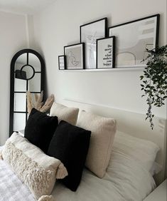 a bed with black and white pillows on top of it next to a plant in a vase