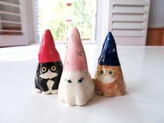 three small ceramic cats wearing hats on top of a white table next to a window