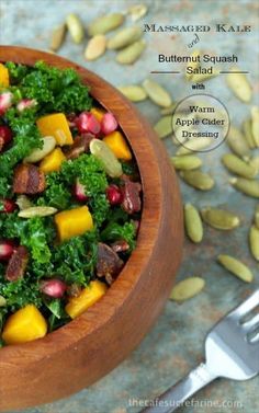 a wooden bowl filled with kale and pomegranates next to a fork