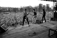 two men standing on stage with microphones in front of an outdoor concert venue full of people