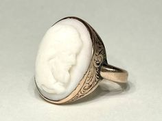 "Beautiful antique cameo ring from the early Victorian era in 10K yellow gold. This very special ring features a beautifully carved high relief cameo carved in white coral, mounted in a sturdy engraved Victorian era bezel mount . The top of the ring measures 19mm north to south. Solid gold bezel, back and ring shank. Ring size 5 1/2 and sizable. Please allow one week for sizing. One month layaway payment plans available on rings $500 and over. Approximate Age - Victorian Gemstone(s) - white coral cameo Metal - 10K Gold Weight - 5 grams Ring size - 5 1/2 Marks - illegible marks Makers Mark - illegible Comments -  Service & Sizing Information: If you require ring sizing or service, kindly follow the link below to add the appropriate service fee from the dropdown menu at the time of purchase. Victorian Oval Carved Rings, White Oval Rings With Intaglio, Antique Cameo Signet Ring For Weddings, Victorian Oval Engraved Carved Ring, Victorian Style Oval Engraved Ring, White Cameo Rings For Wedding, White Cameo Wedding Rings, Antique Carved White Jewelry, Formal White Cameo Rings