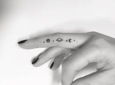 a woman's hand with a small tattoo on the middle finger, and planets