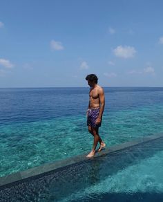 a man standing on the edge of a pier looking out at the blue water in front of him