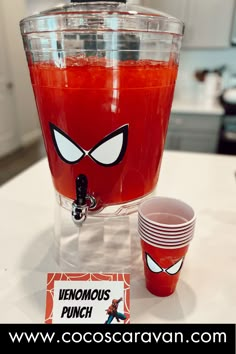 a drink dispenser sitting on top of a counter next to two cups