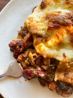 a white plate topped with lasagna covered in meat and cheese next to a fork