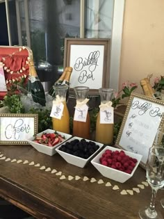 a table topped with different types of fruit and drinks next to framed signs that say bubbly bar