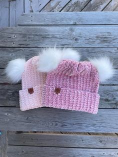 two pink and white knitted hats with pom - poms sitting on top of each other