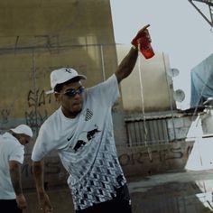 a man in white shirt and black shorts holding up a red bottle with one hand