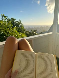 a person is reading a book while sitting in a chair on a balcony overlooking the city