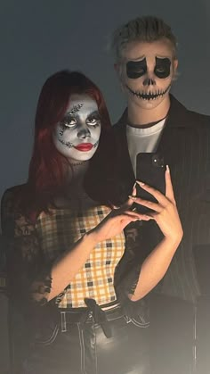 two people dressed up in costumes and makeup are holding their cell phones while looking at the screen