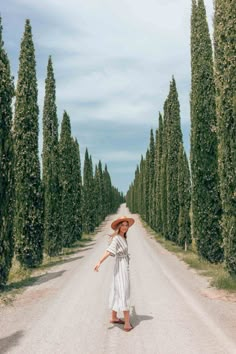 a woman standing in the middle of an empty road surrounded by tall, slender trees